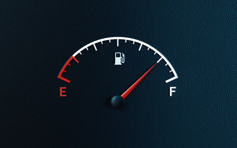 Fuel gauge's red needle indicating full gas tank on black background. Horizontal composition with copy space.
