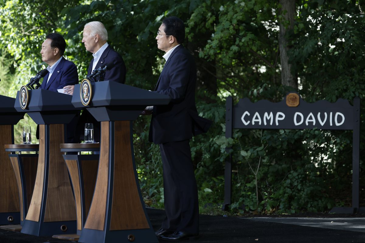 Japanese Prime Minister Fumio Kishida, Joe Biden, and South Korean President Yoon Suk Yeol stand at podiums in front of a “Camp David” sign.