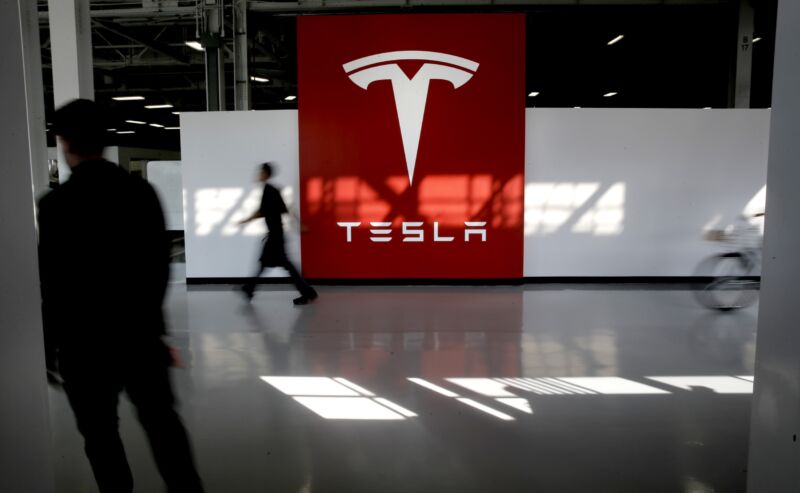 Workers walk past a large Tesla logo.