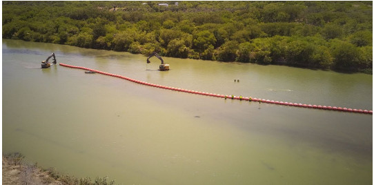 A muddy river with a long orange line of floats in the middle running parallel to the shore.