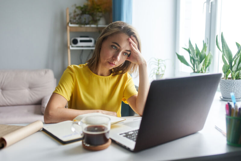 A woman in a bright yellow jacket is sitting in front of a laptop in emotional tension.