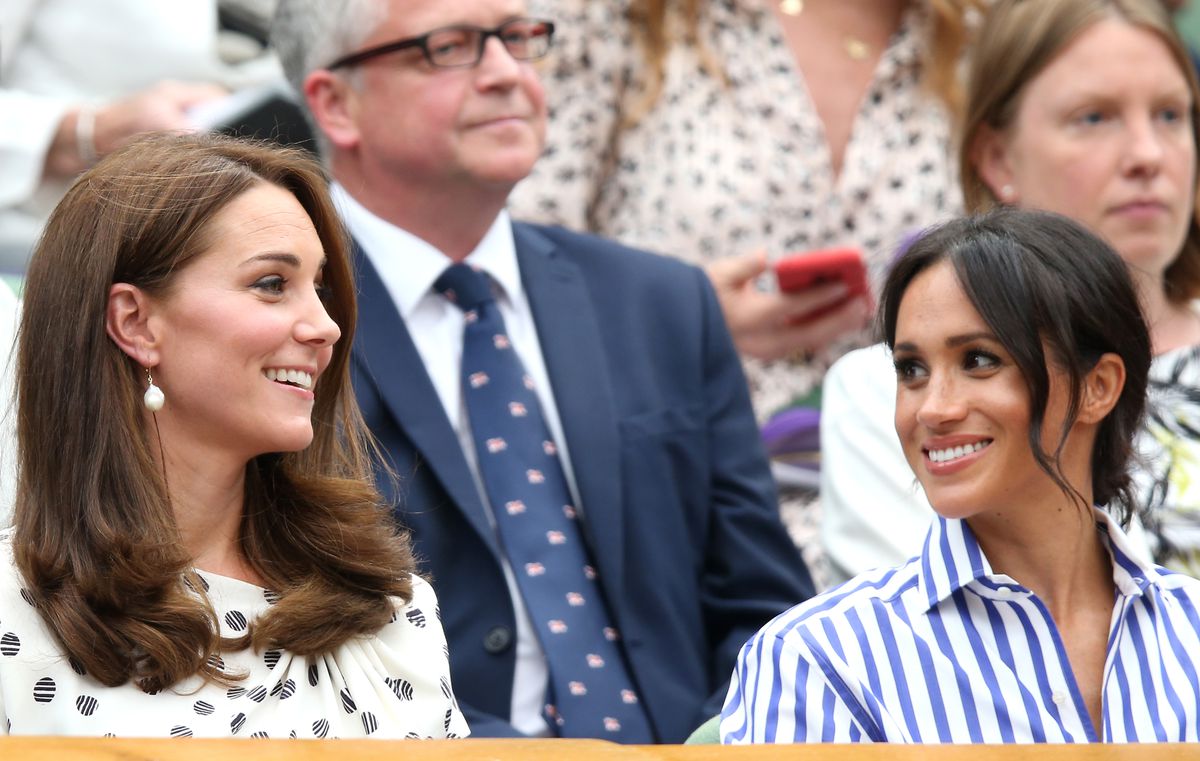 Two women, Kate and Meghan, sit smiling at each other on a set of bleachers. On the left, Kate has her hair down and smooth and is wearing a polka dot dress. On the right, Meghan has her hair in a loose bun and is wearing a striped shirt.