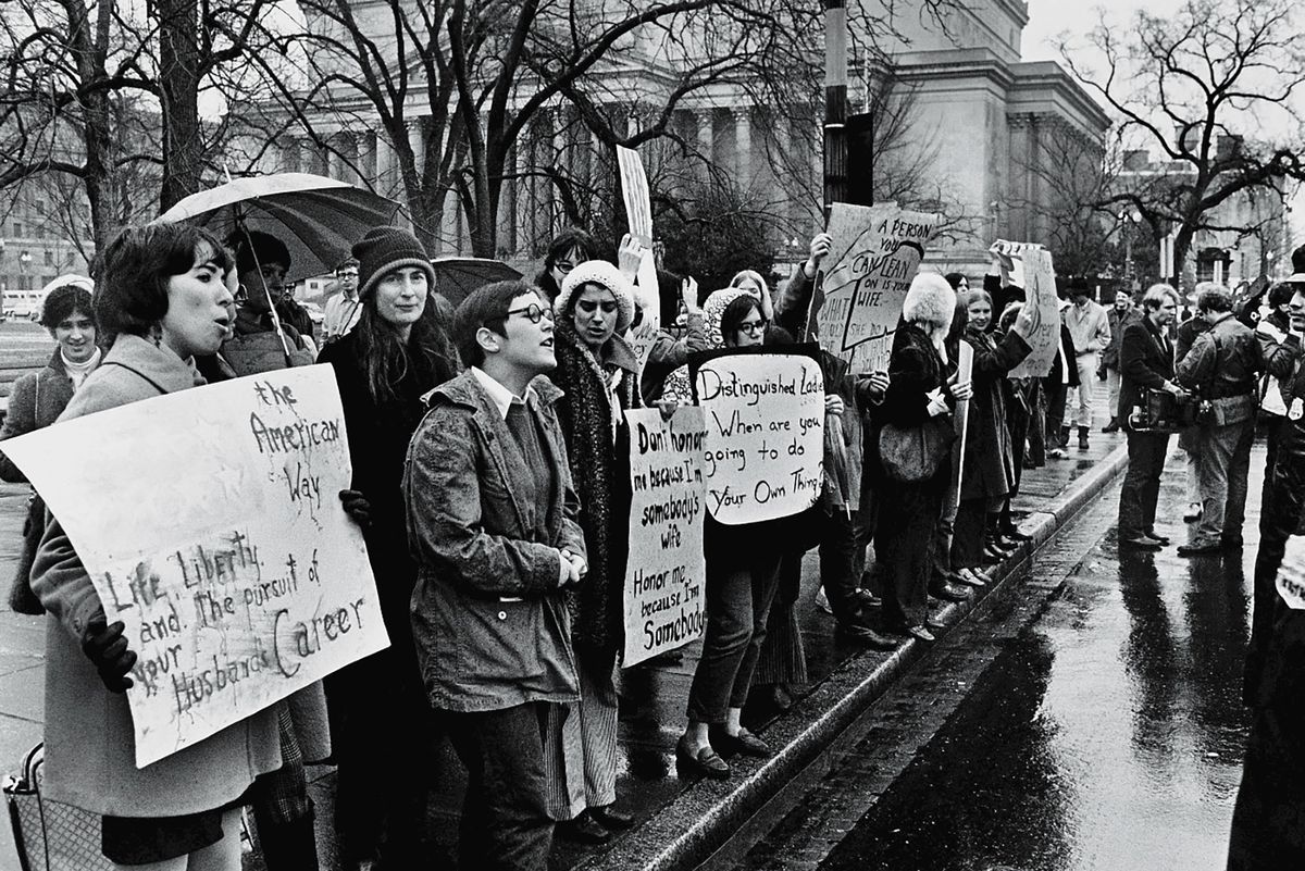 Black-and-white photo of a group of young American women protesting in the rain for women’s rights as police look on along the street near a government building during Richard Nixon’s presidential inauguration weekend, Washington, DC, January 18-21, 1969.
