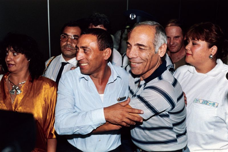 Two middle-aged men embrace in a crowd of others.