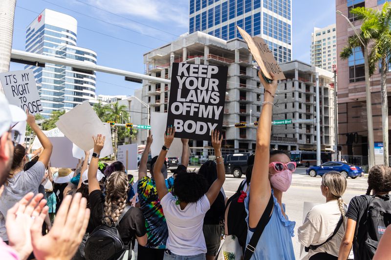 Abortion rights activists and protesters hold signs on a Fort Lauderdale city street corner, including “Keep your laws off my body” and “It’s my right to choose.”