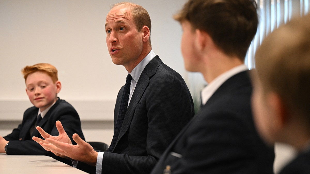 Prince William sitting next to Freddie while addressing students.
