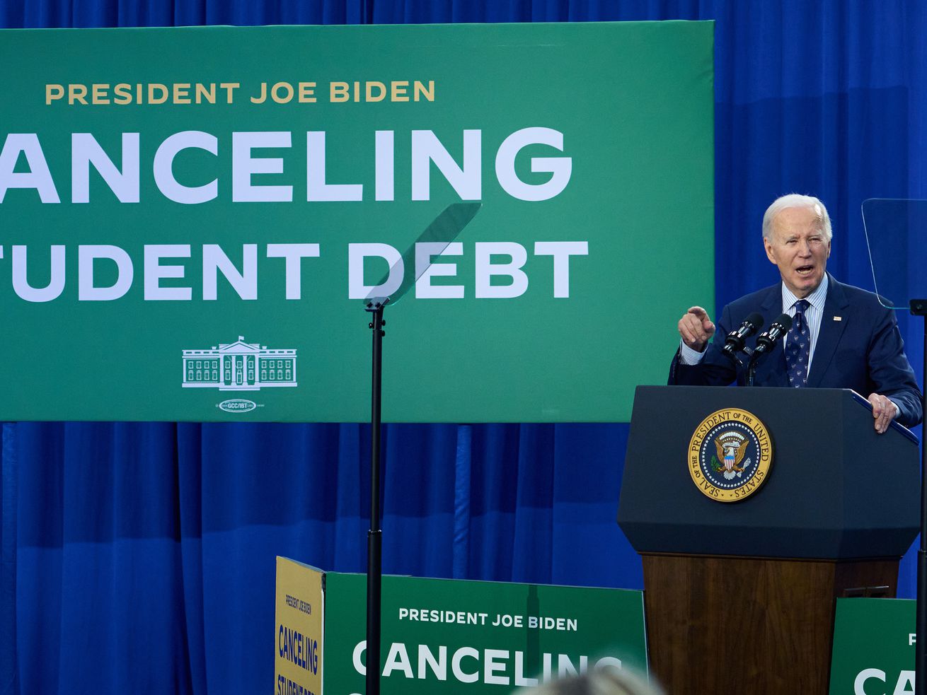 President Biden speaks onstage at a lectern beside a screen that reads “canceling student debt.”