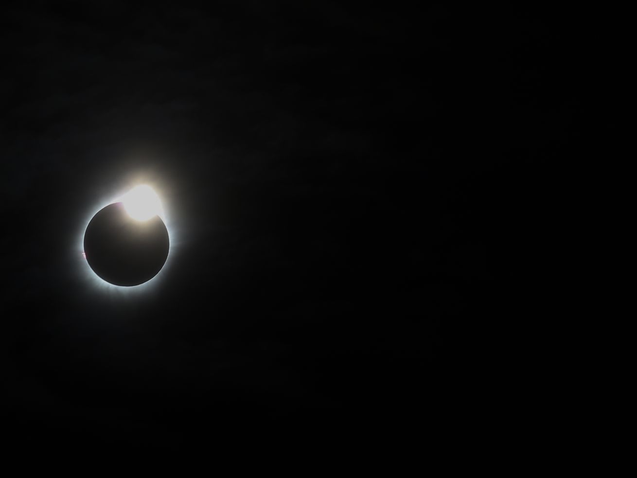 The eclipsed sun, a black circle surrounded by a glowing white corona, hangs in a black sky.