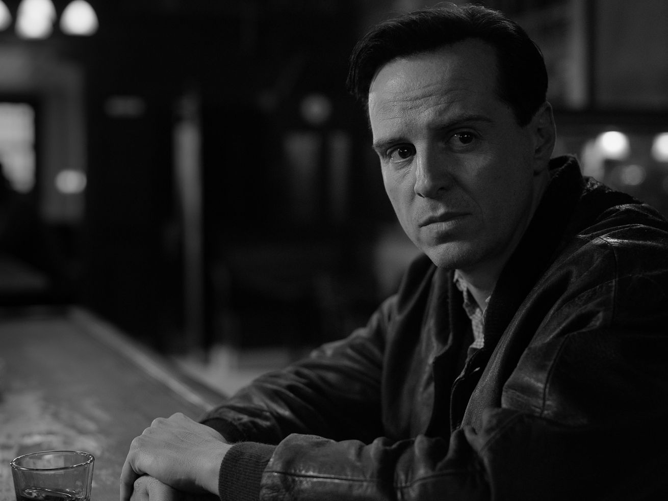 A black-and-white still of a man sitting at a bar counter, looking somber.