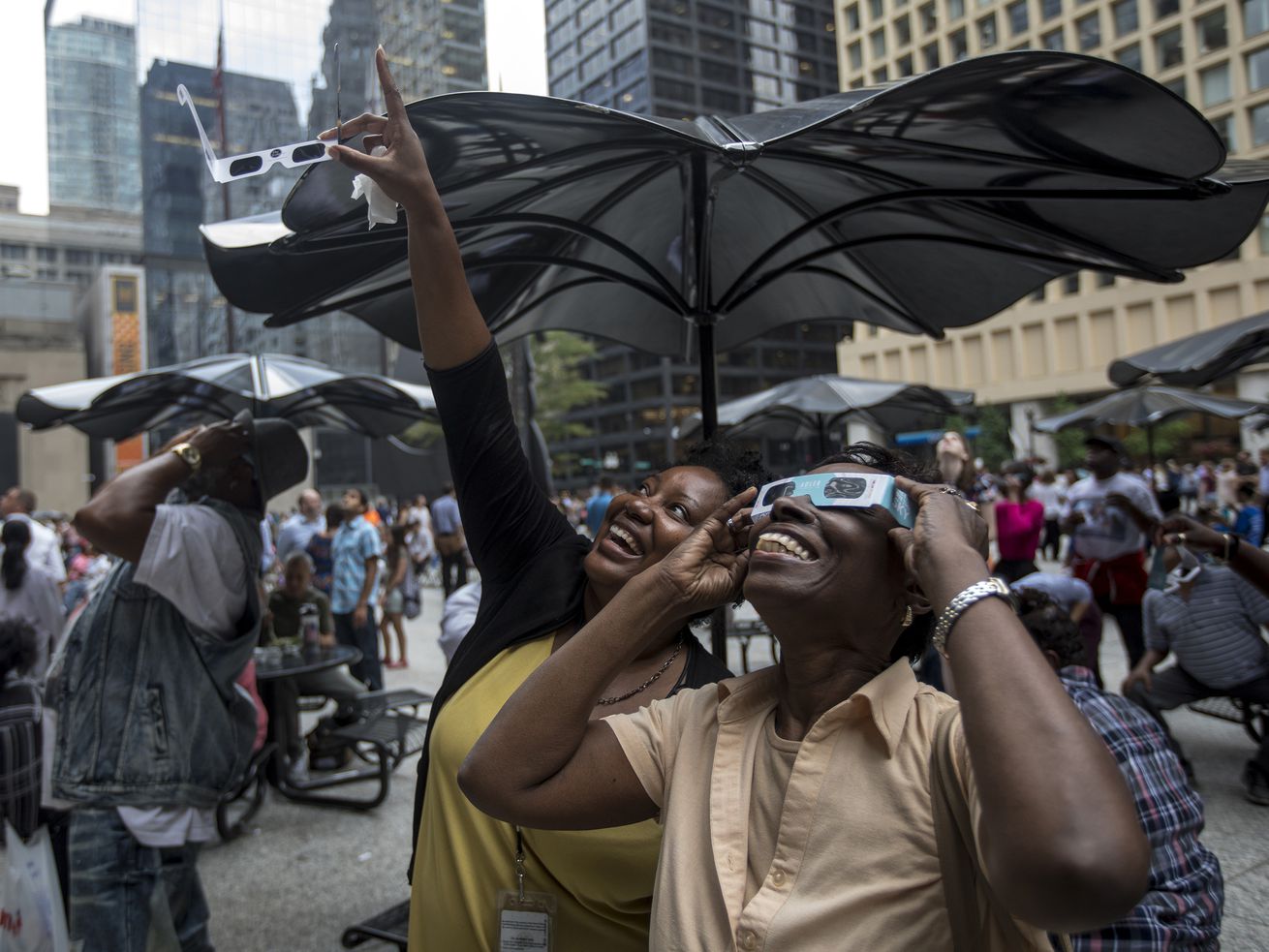 people in an outdoor crowd wear eclipse glasses and point to the sky.