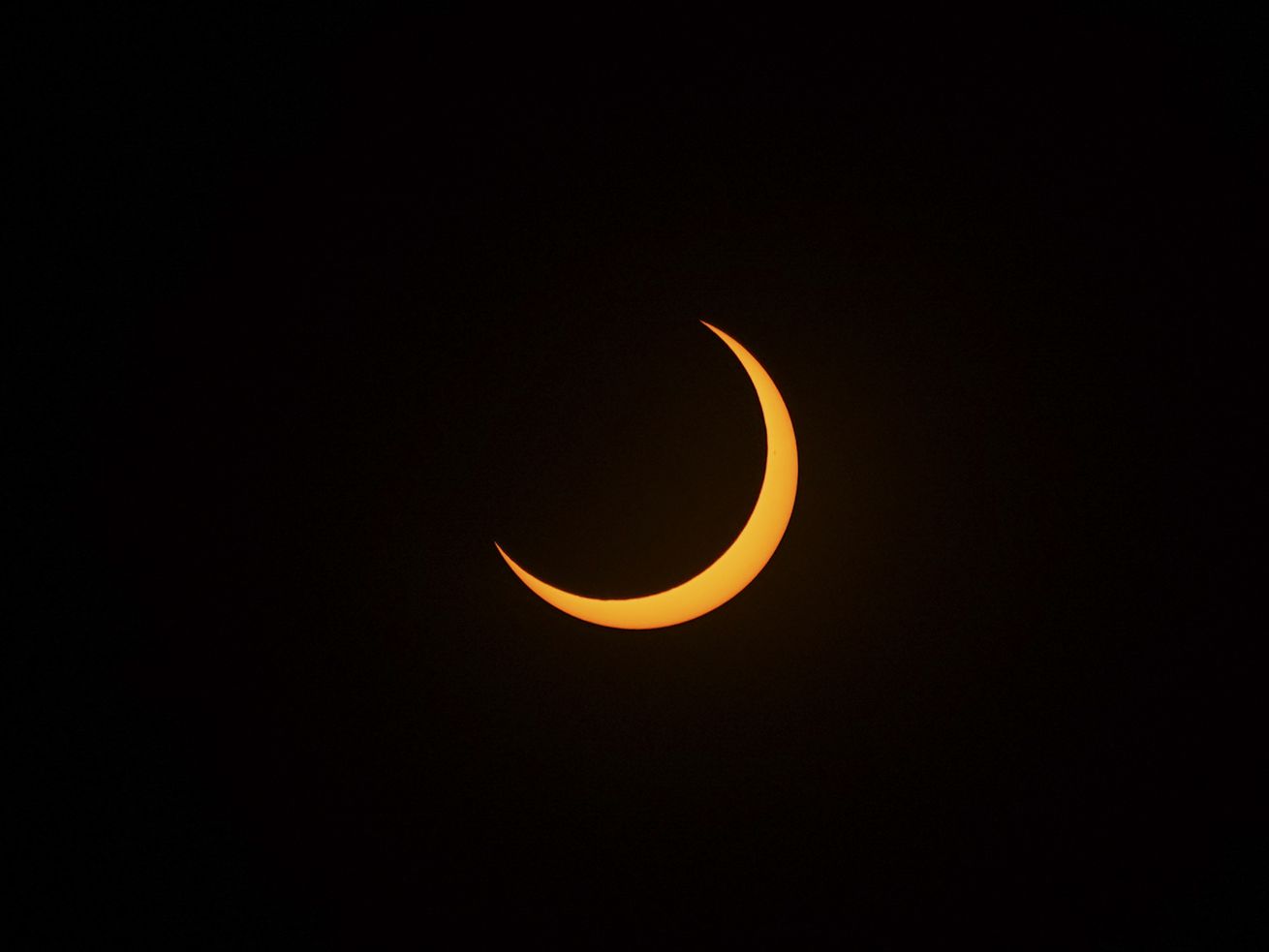 A partial solar eclipse that shows a crescent-shaped rim of the sun against a black sky.