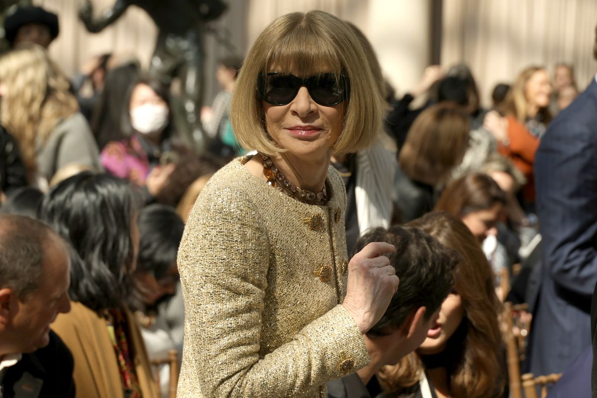 Anna Wintour, in her signature black sunglasses and a tan Chanel-style suit, walks up the Met steps.