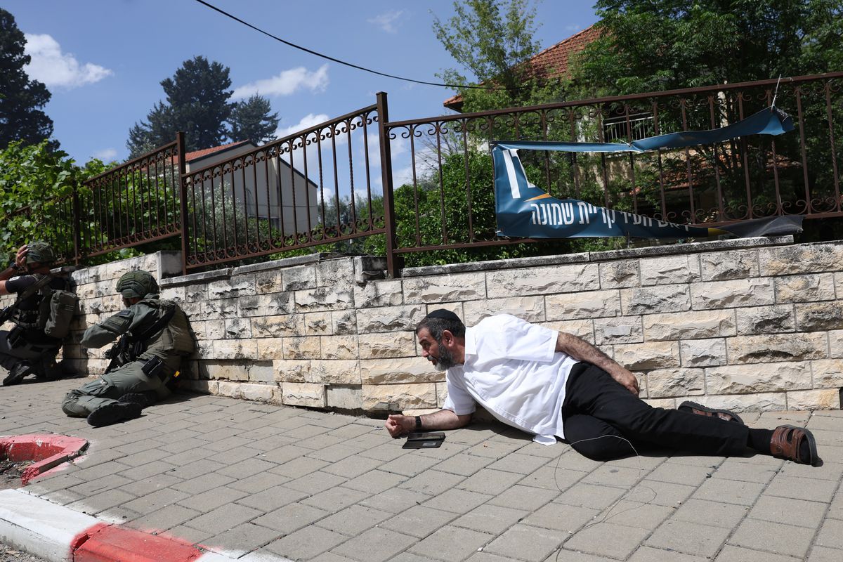 A man lies on the sidewalk behind armed soldiers.