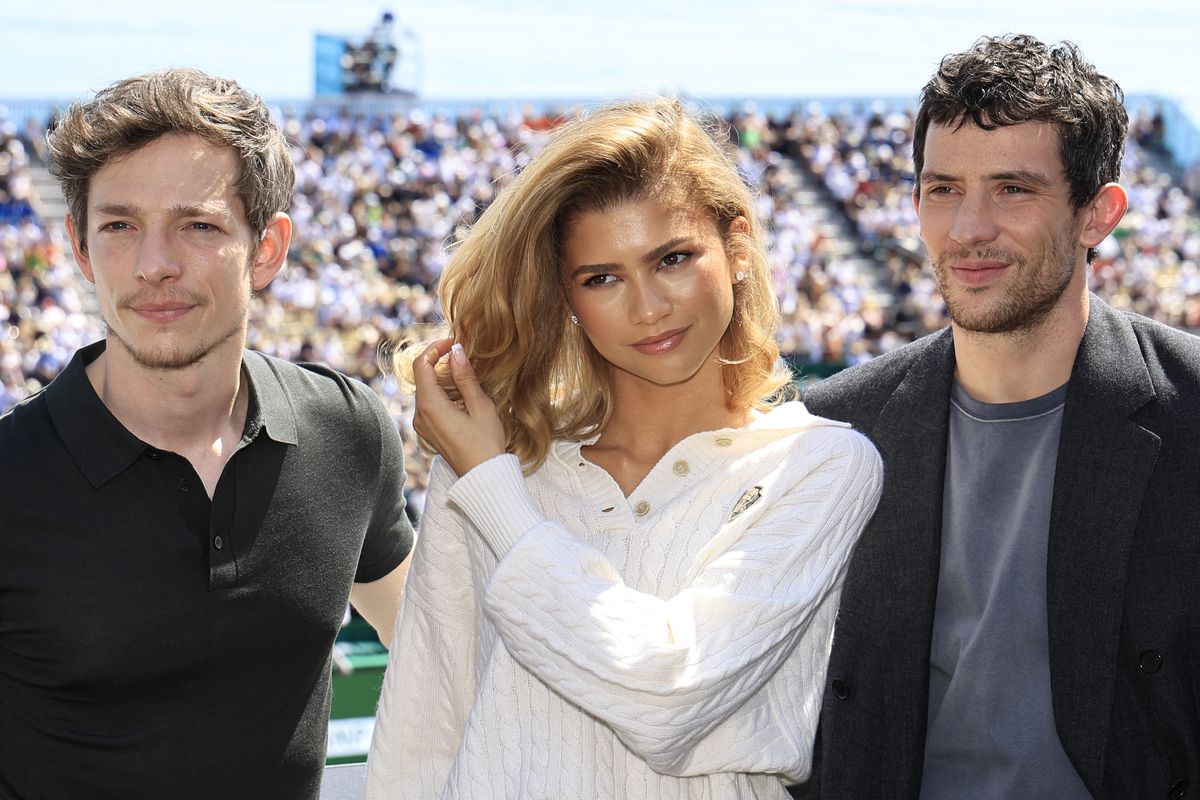 Actors Mike Faist, Zendaya, and Josh O’Connor, from left to right, pose during promotional photos in front of a tennis court.