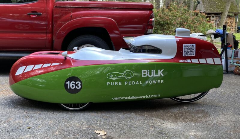 Image of a aerodynamic recumbent bicycle parked in front of a pickup truck.