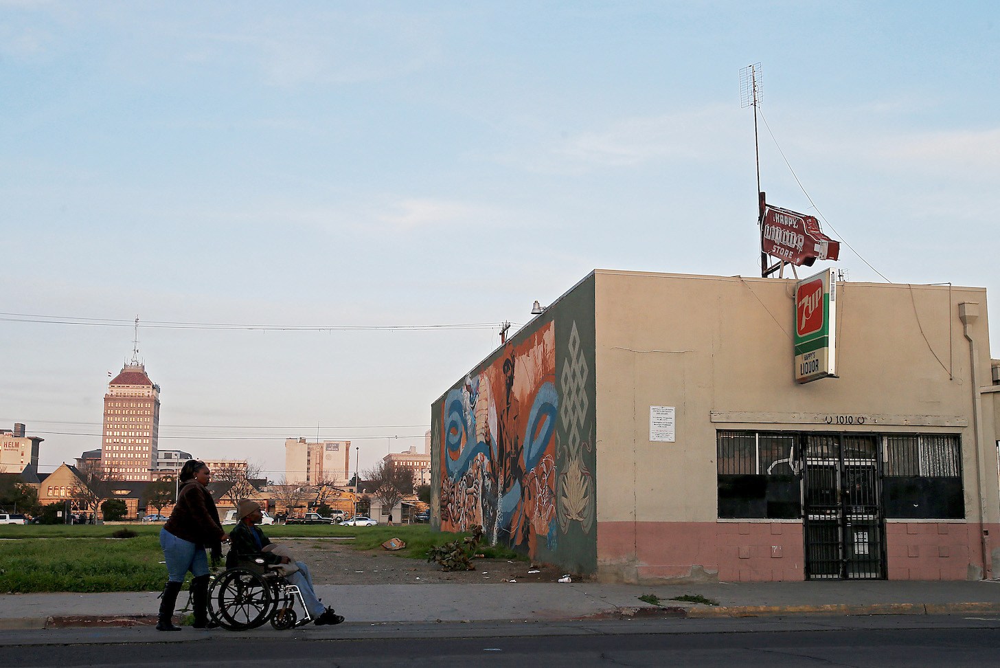 A person pushes another person in a wheelchair past a shuttered storefront in Fresno.