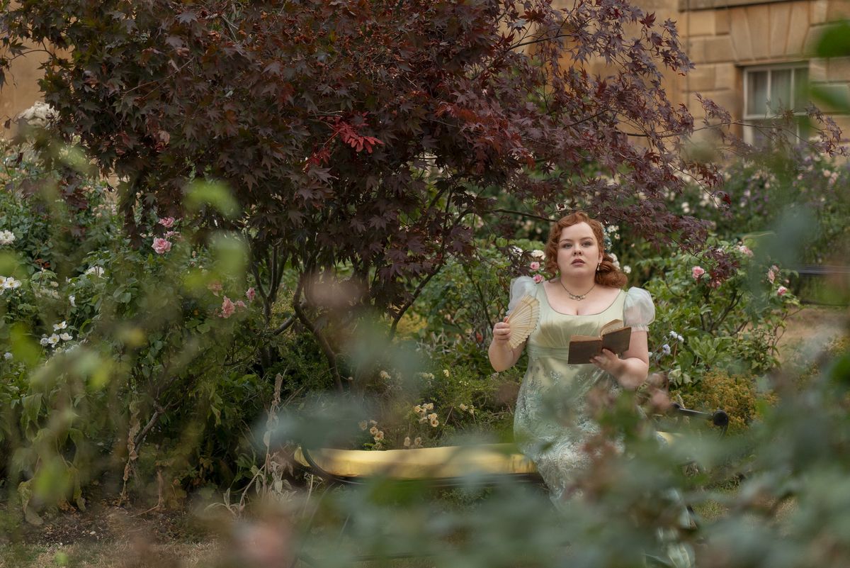 Bridgerton’s Penelope in a garden. holding a book.