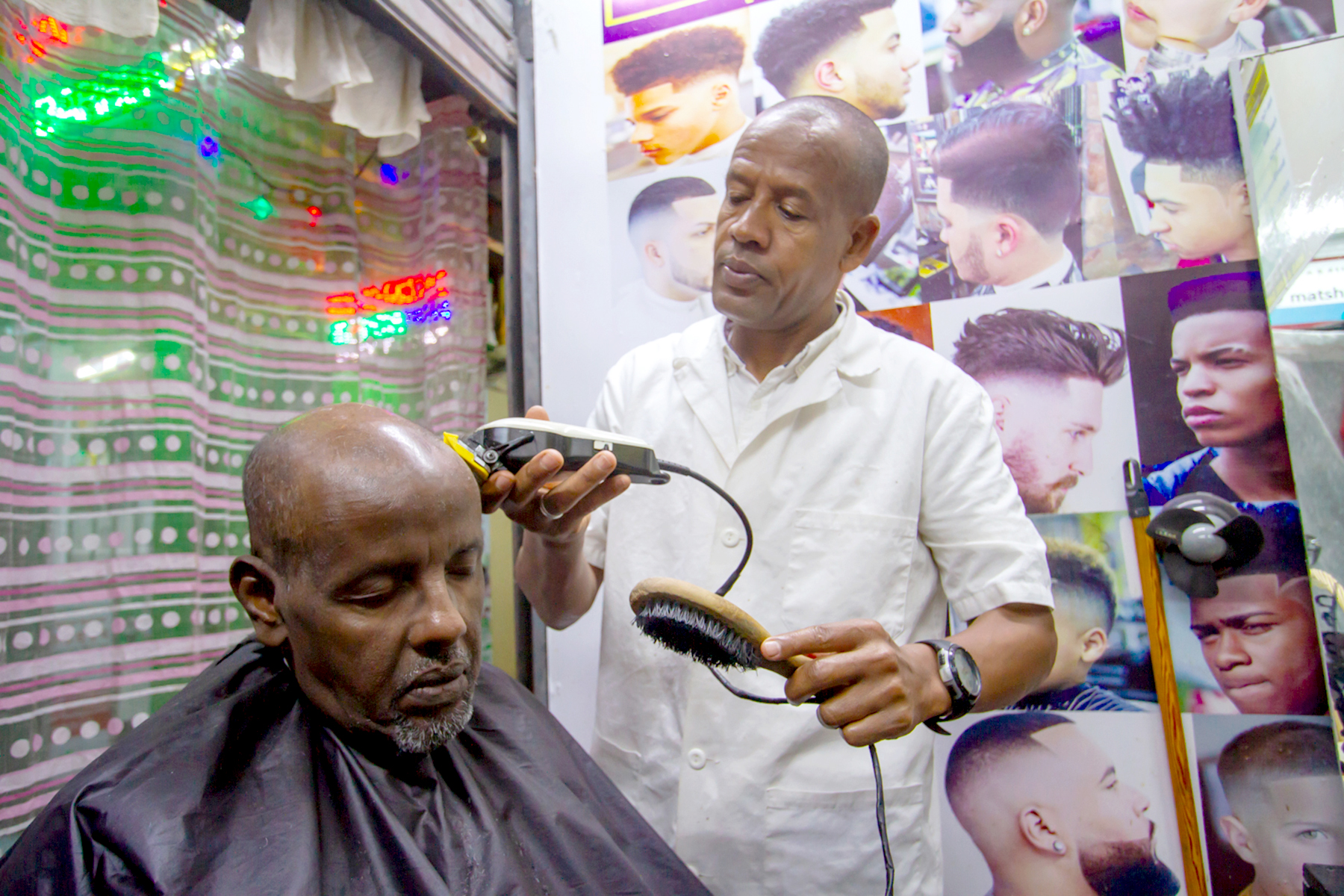 Matthewos Shifa, 47, a refugee from Ethiopia, uses the cash to open a barber shop. Here he gives a haircut to Abdi Shire, a businessman from Somalia staying at a hotel down the street in the popular immigrant neighborhood of Eastleigh.
