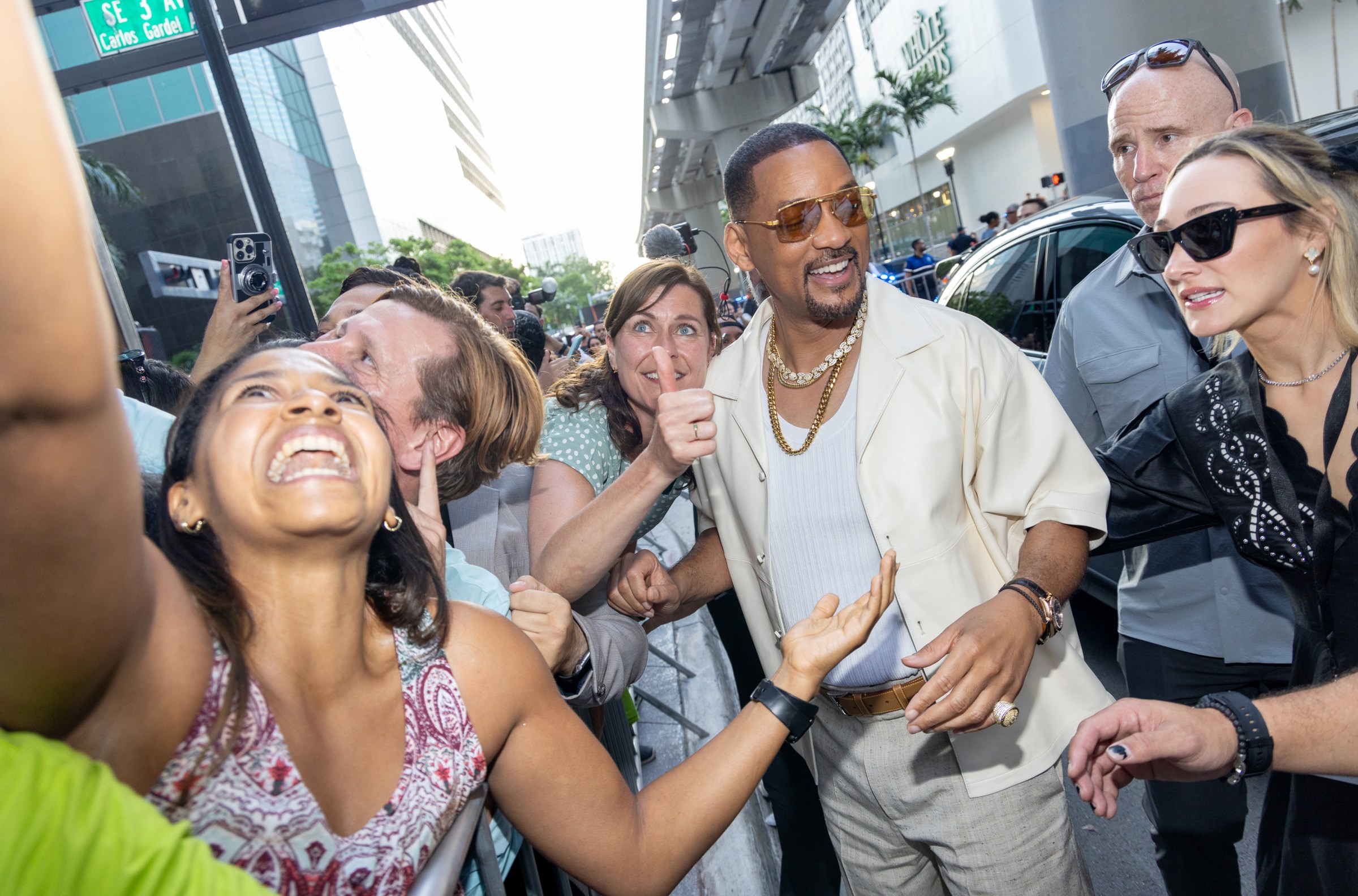 Will Smith walks close by fans, who lean back to take selfies with him.