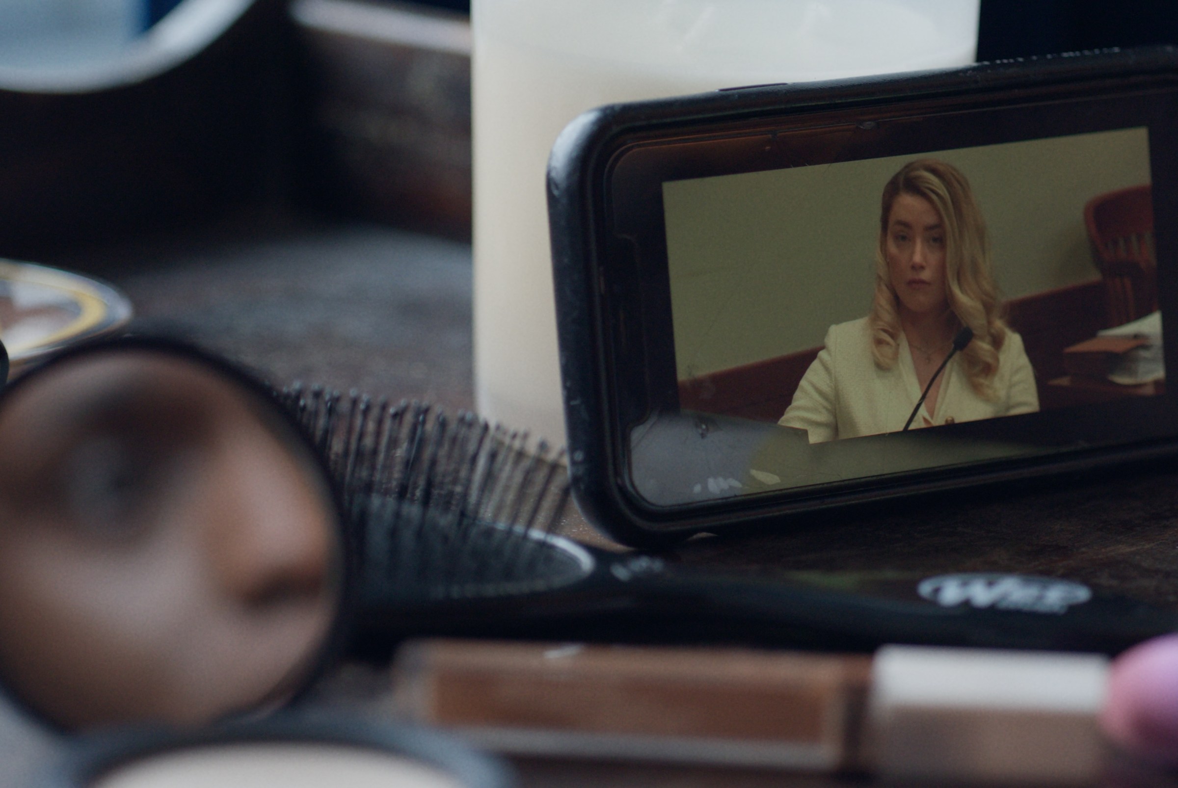 A camcorder screen showing a blonde woman on a witness stand.