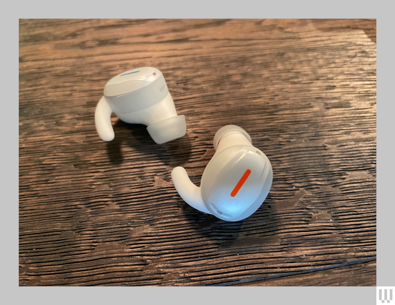 Two white inear hearing aids sitting on a wooden surface