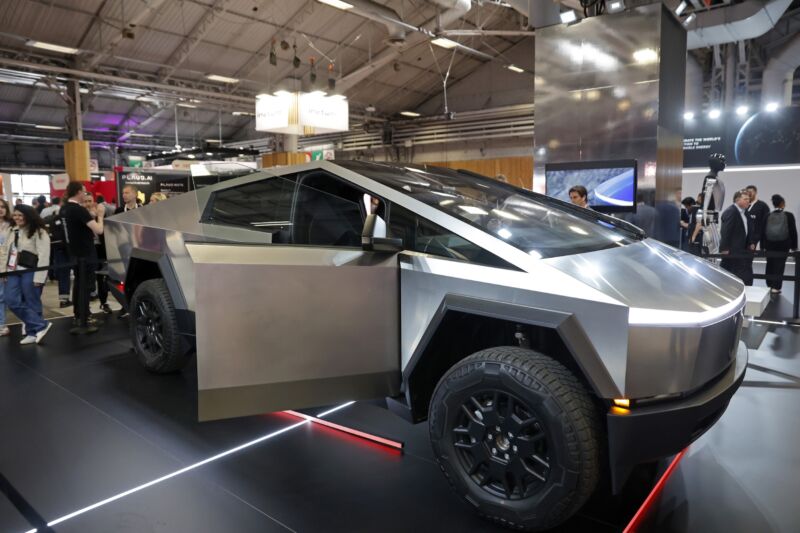 A Tesla Cybertruck with the passenger door open is displayed in a convention center.