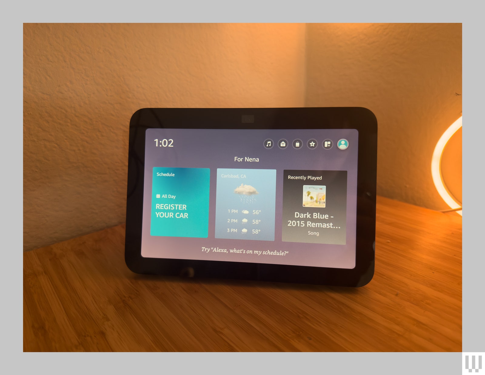 Tabletlike device sitting on wooden surface in the corner of a room. The screen displays a schedule the weather and...