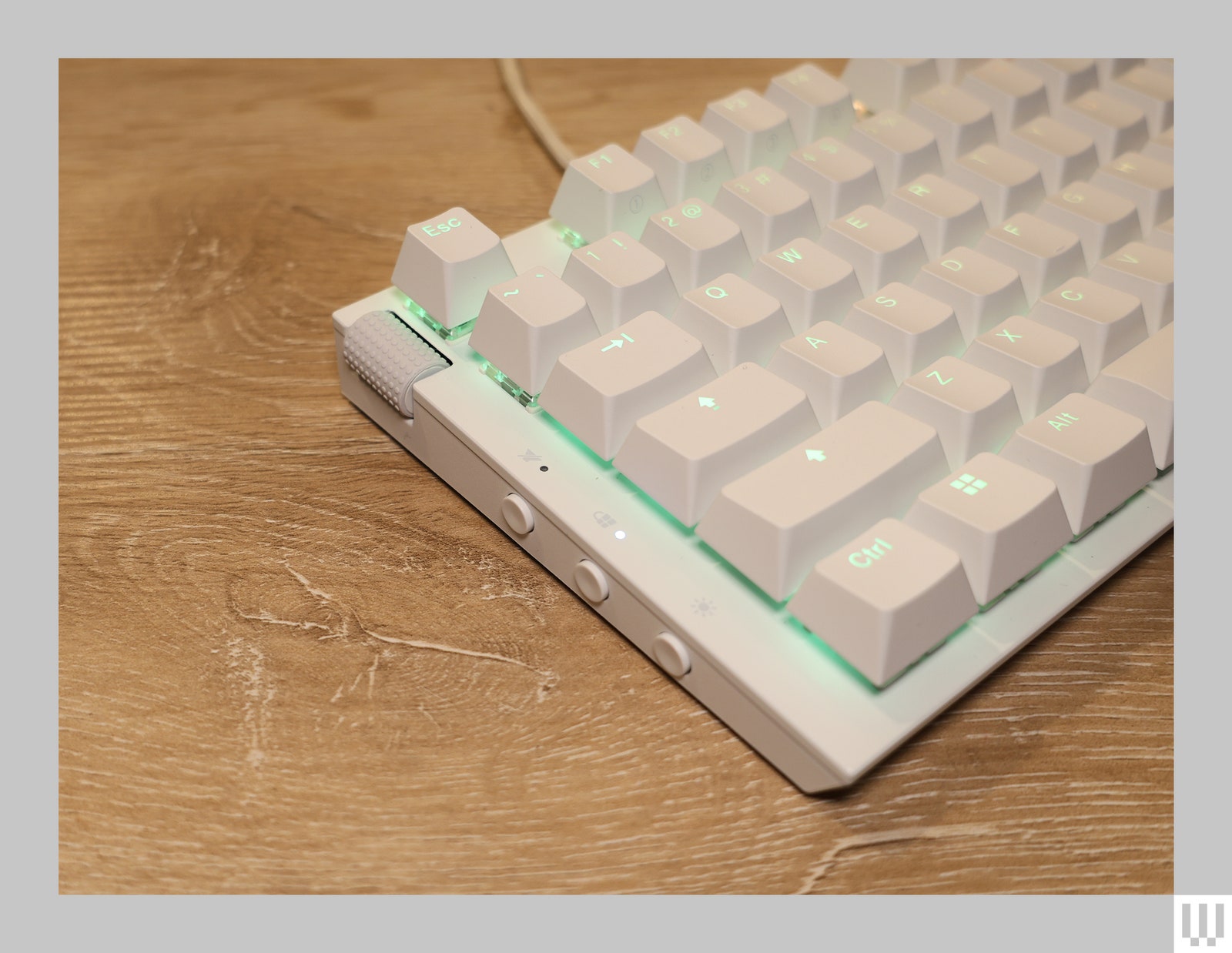 Closeup of the left side of white computer keyboard with illuminated keys and a wheel on the top left