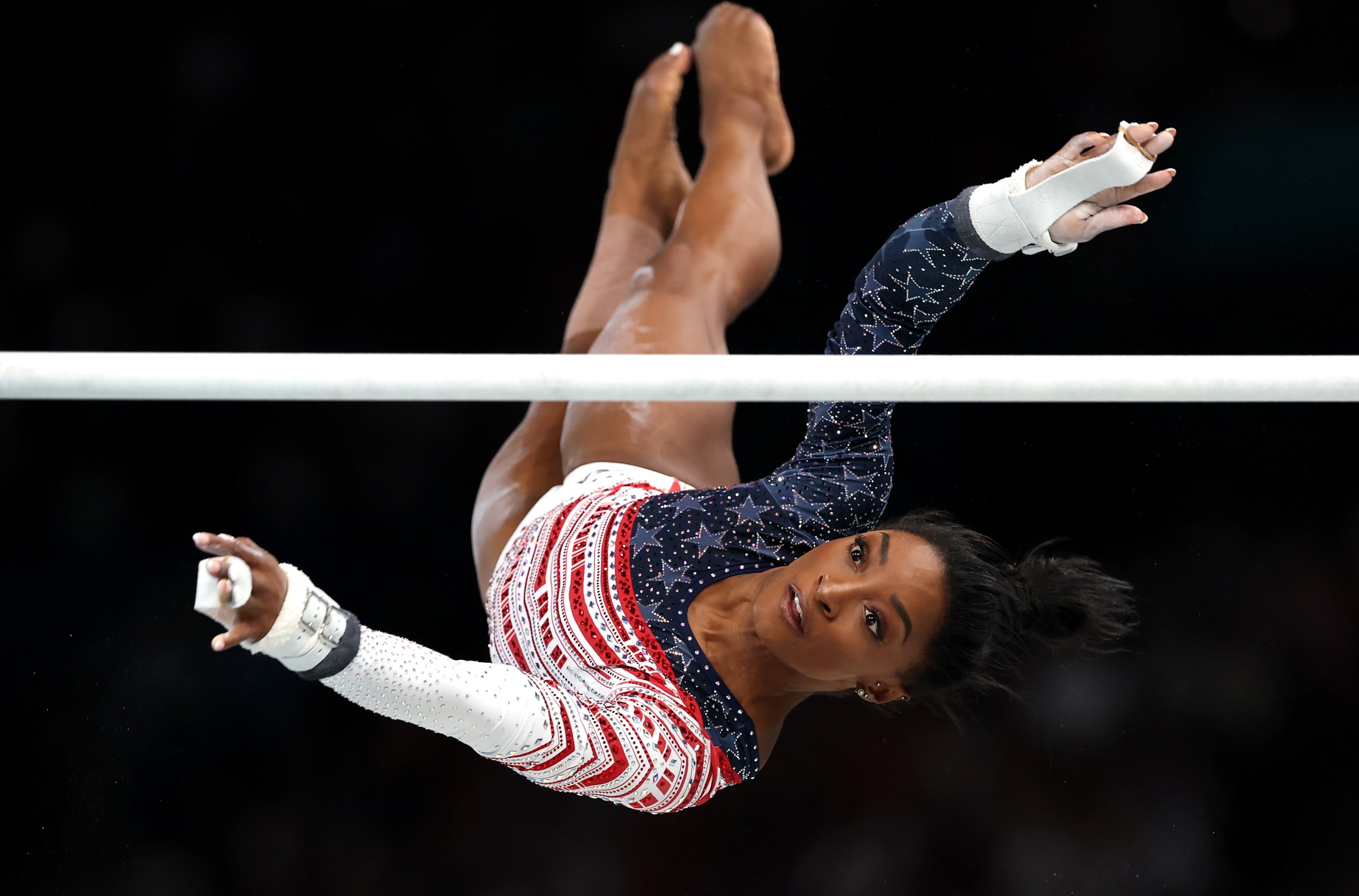 A gymnast in mid-air with her eyes on the bar she is going to grasp.