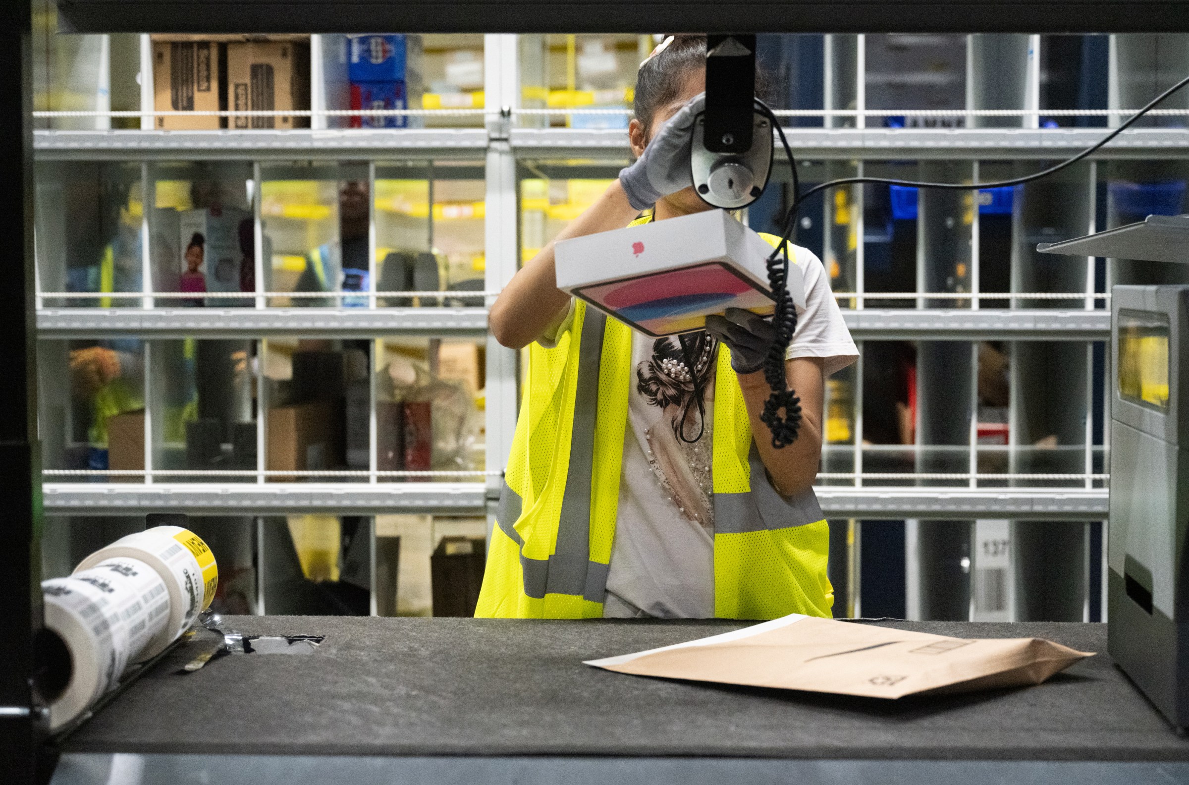 A person wearing a yellow safety vest scans an apple-branded package in a warehouse.