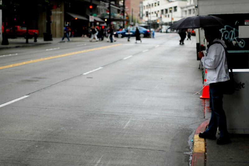 a person on a sidewalk in downtown Seattle, preparing to jaywalk across the street.