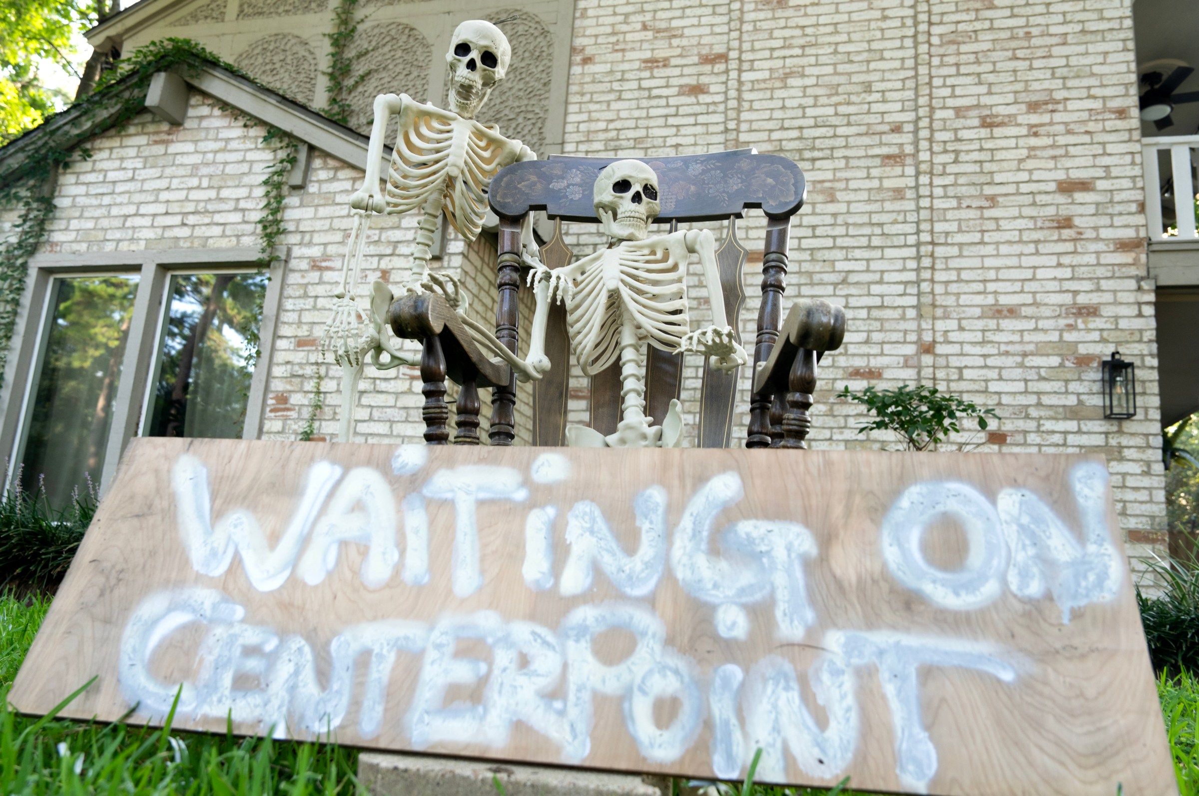 A pair of plastic skeletons along with a sign that reads "Waiting on Centerpoint" is seen in the front yard of a Houston home.