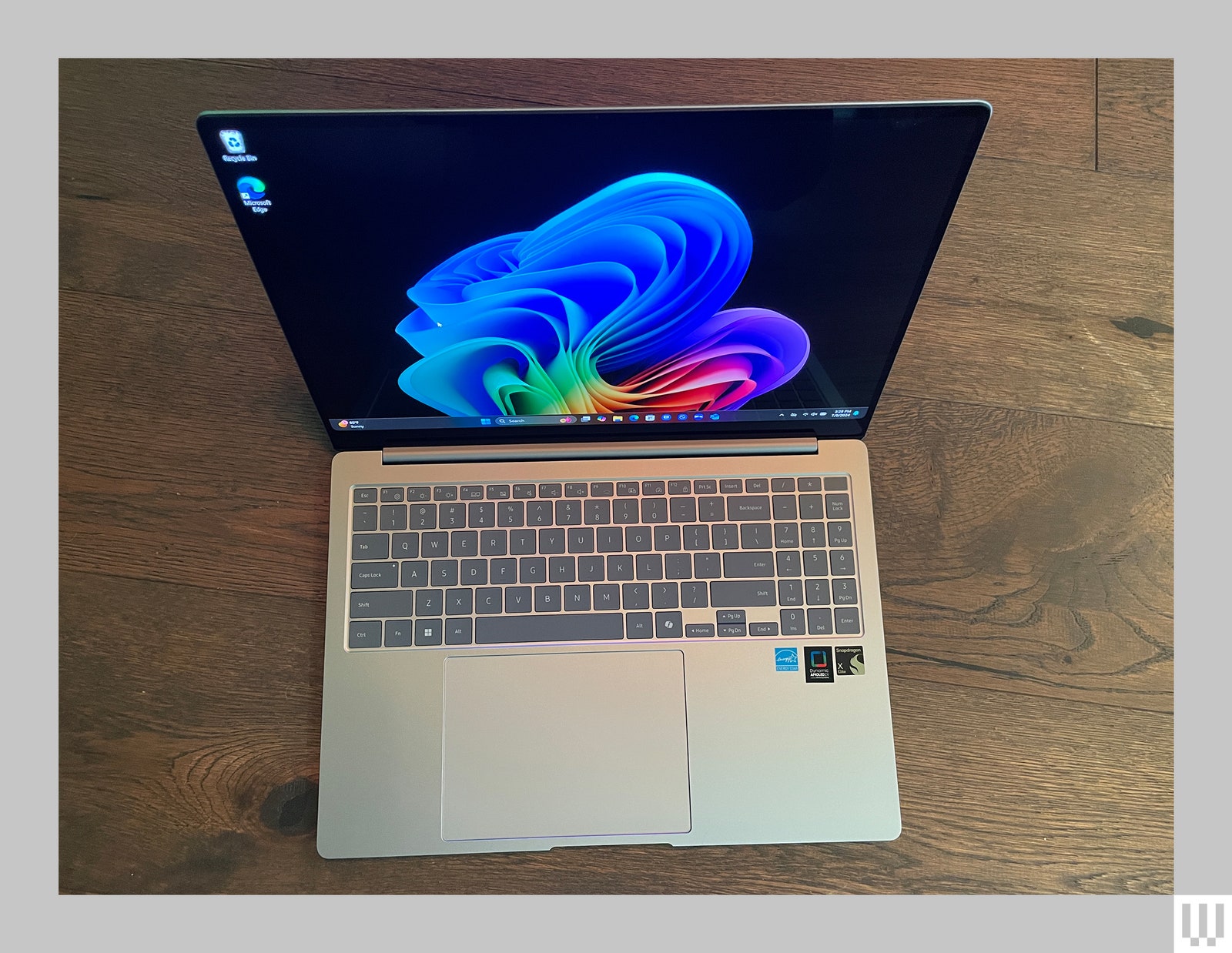 Topdown view of opened silver laptop showing the keyboard and abstract art on thes screen