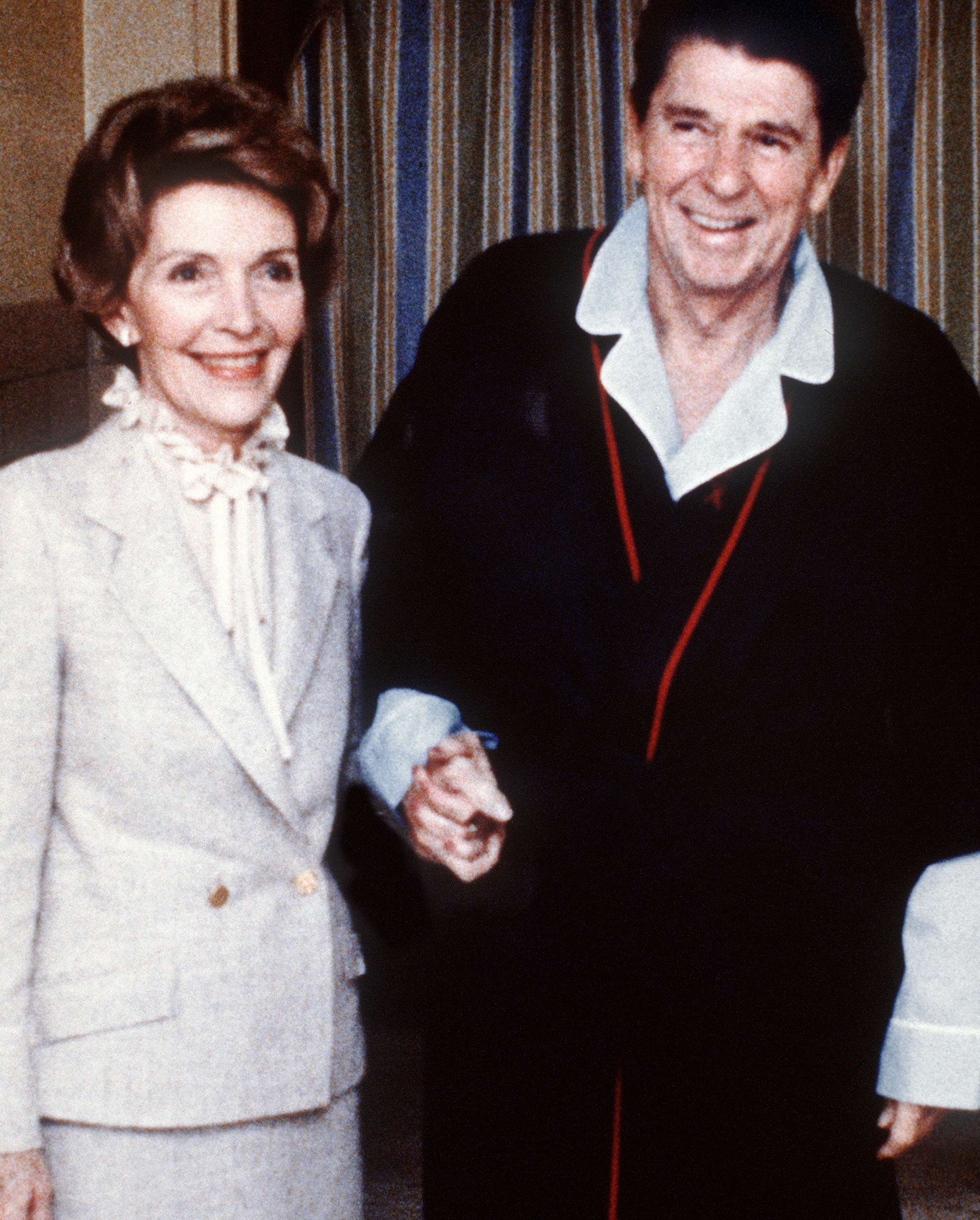 In a 1981 photo, Ronald and Nancy Reagan, both in suits and coats, hold hands outside a hospital.