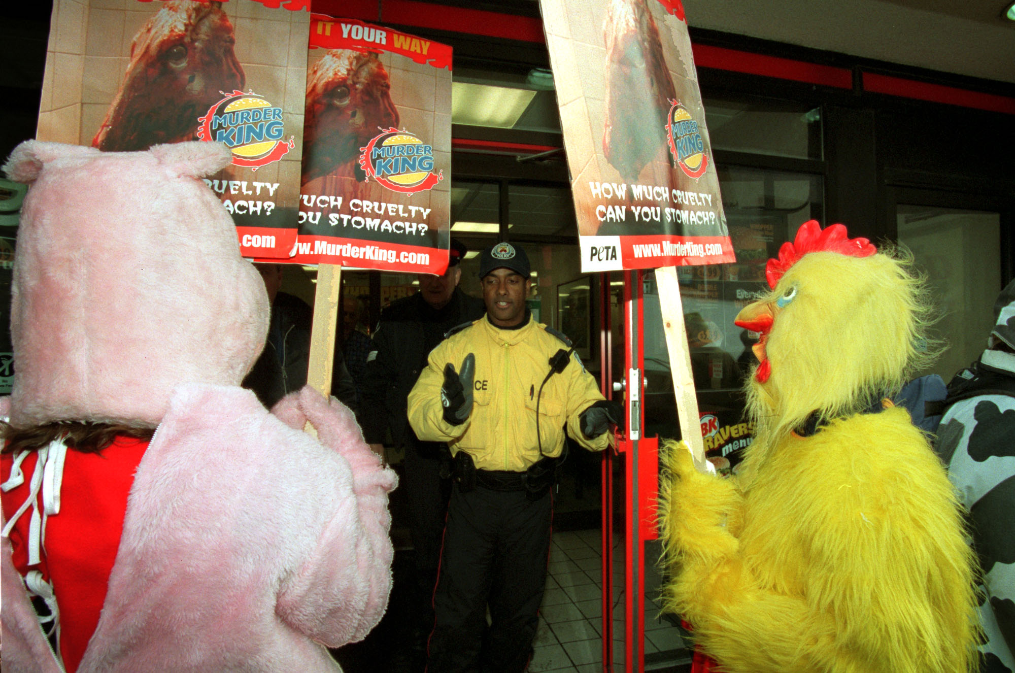 Two protesters, one dressed as a chicken and one dressed as a pig, hold up signs protesting “Murder King”