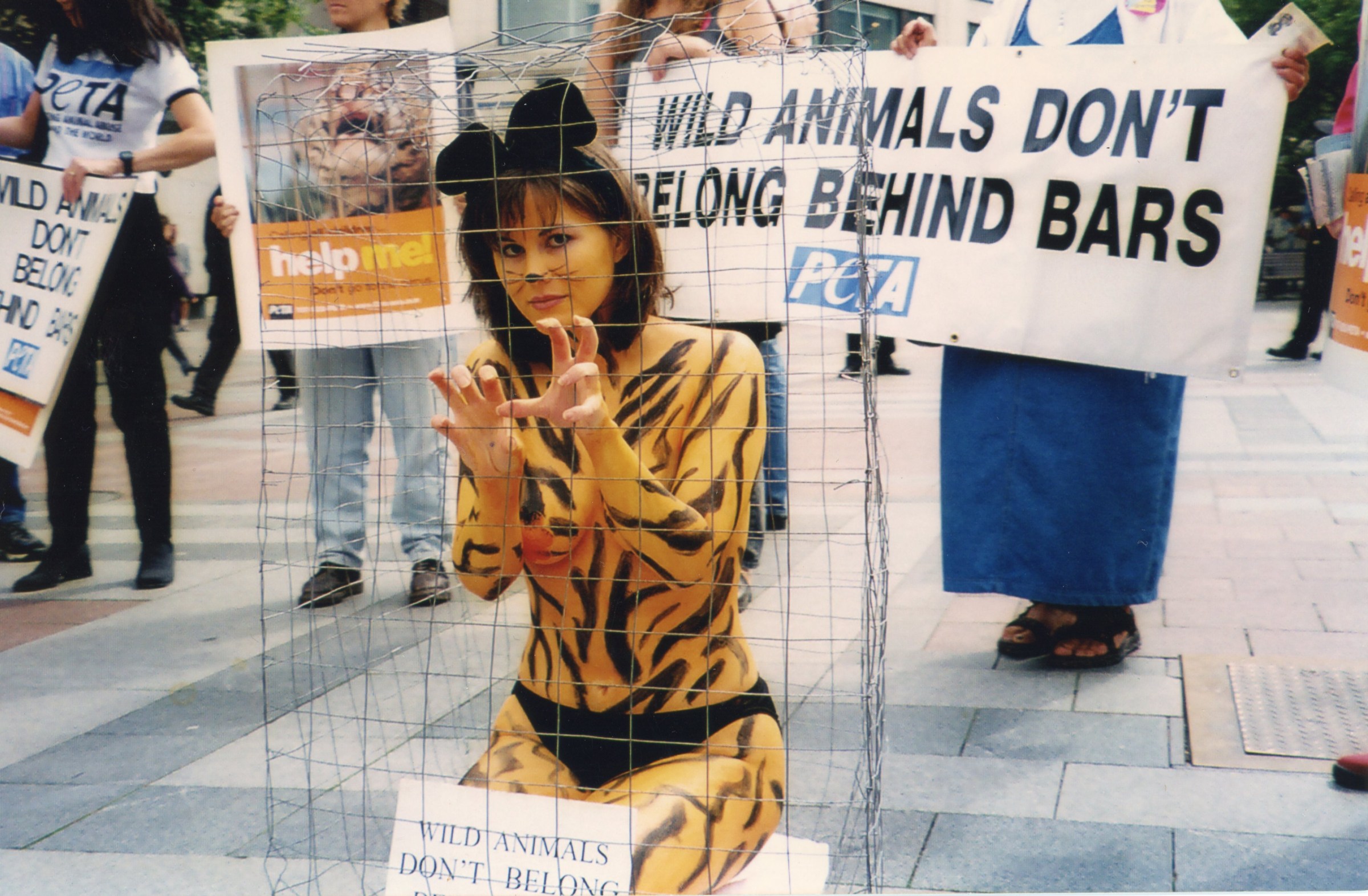 A woman painted with tiger stripes sits in a cage protesting the use of animals in circuses. A protester behind her holds a sign reading “WILD ANIMALS DON’T BELONG BEHIND BARS.”