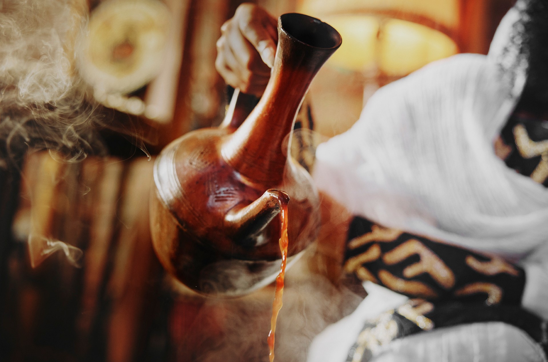 A photo of a woman pouring coffee from a jebena