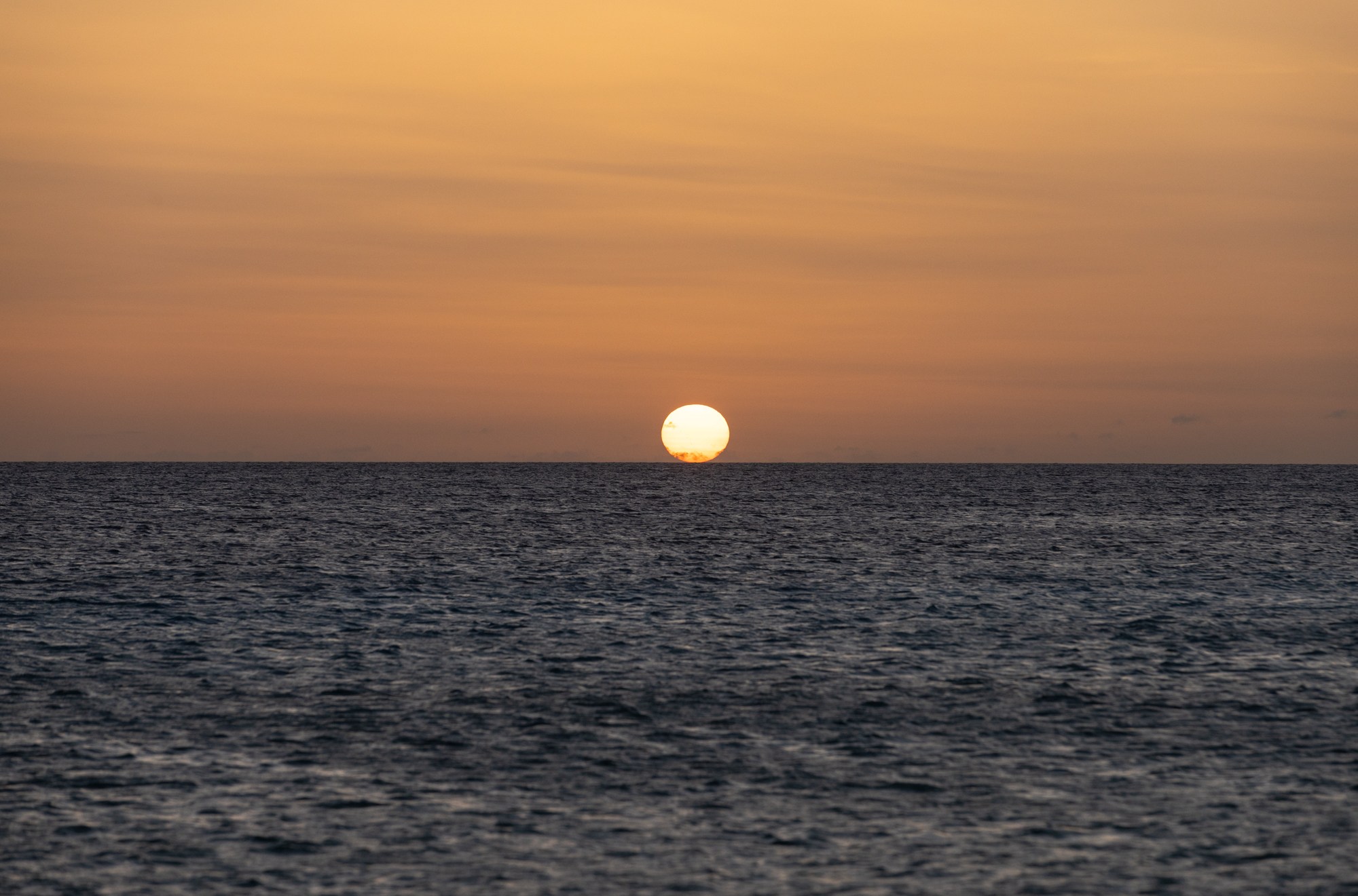 An orange sun setting over the ocean