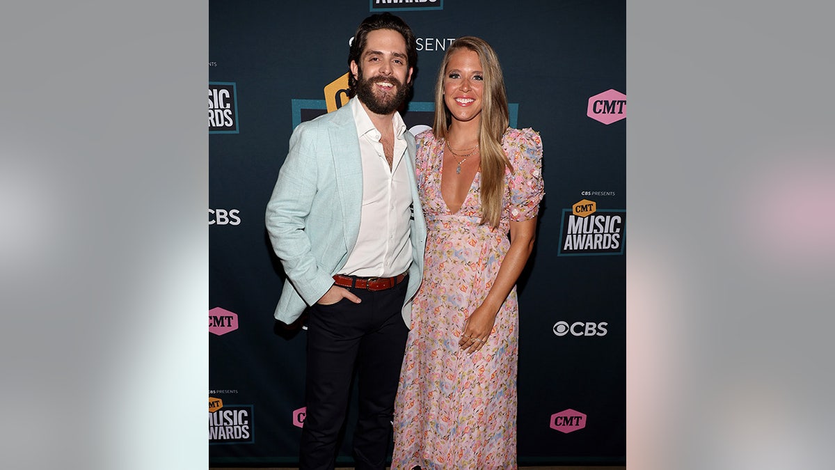 Thomas Rhett smiles in an icy blue suit next to his wife Lauren in a patterned pink dress on the carpet