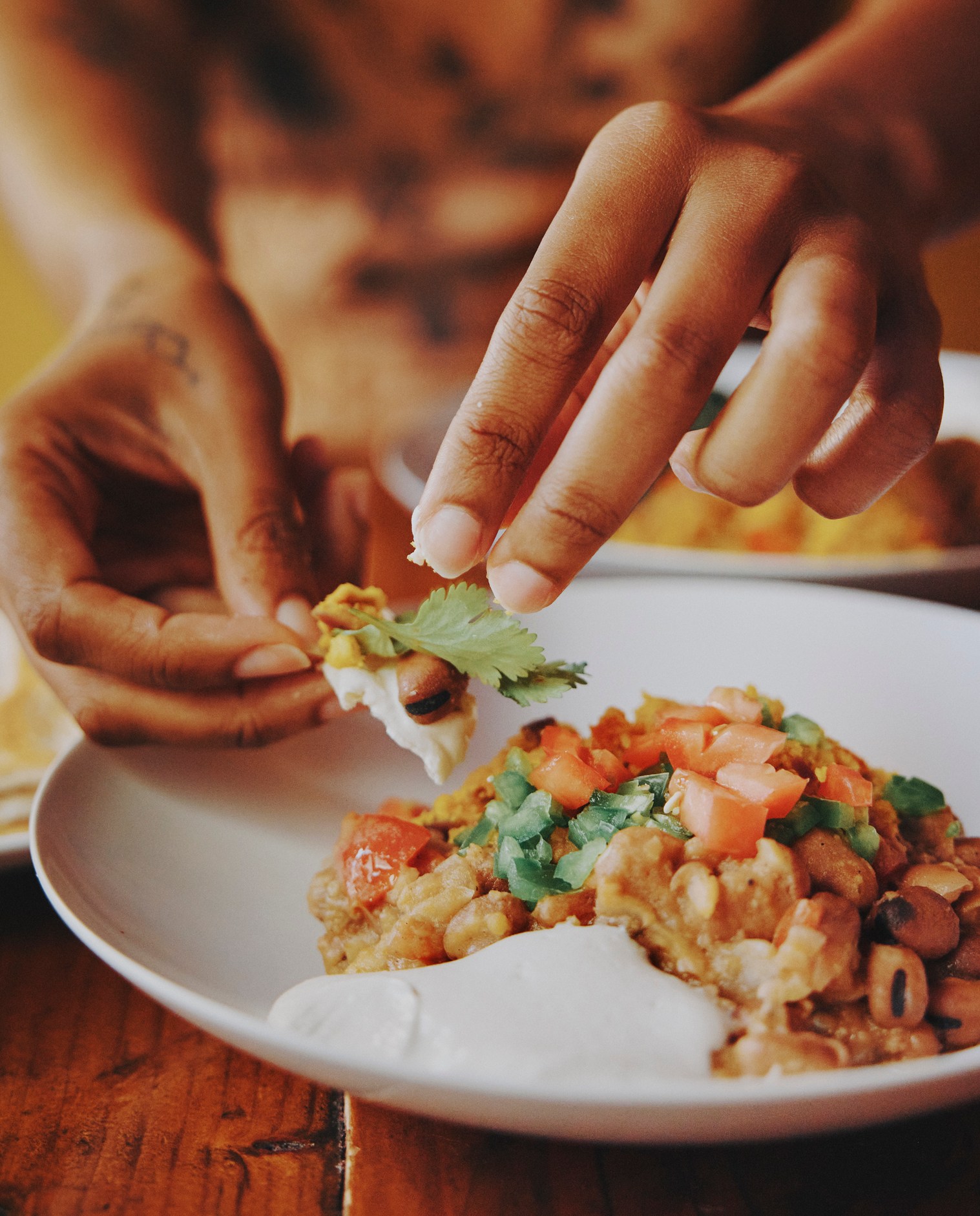 A photo of hands carefully prepares a bite of food containing beans and vegetables