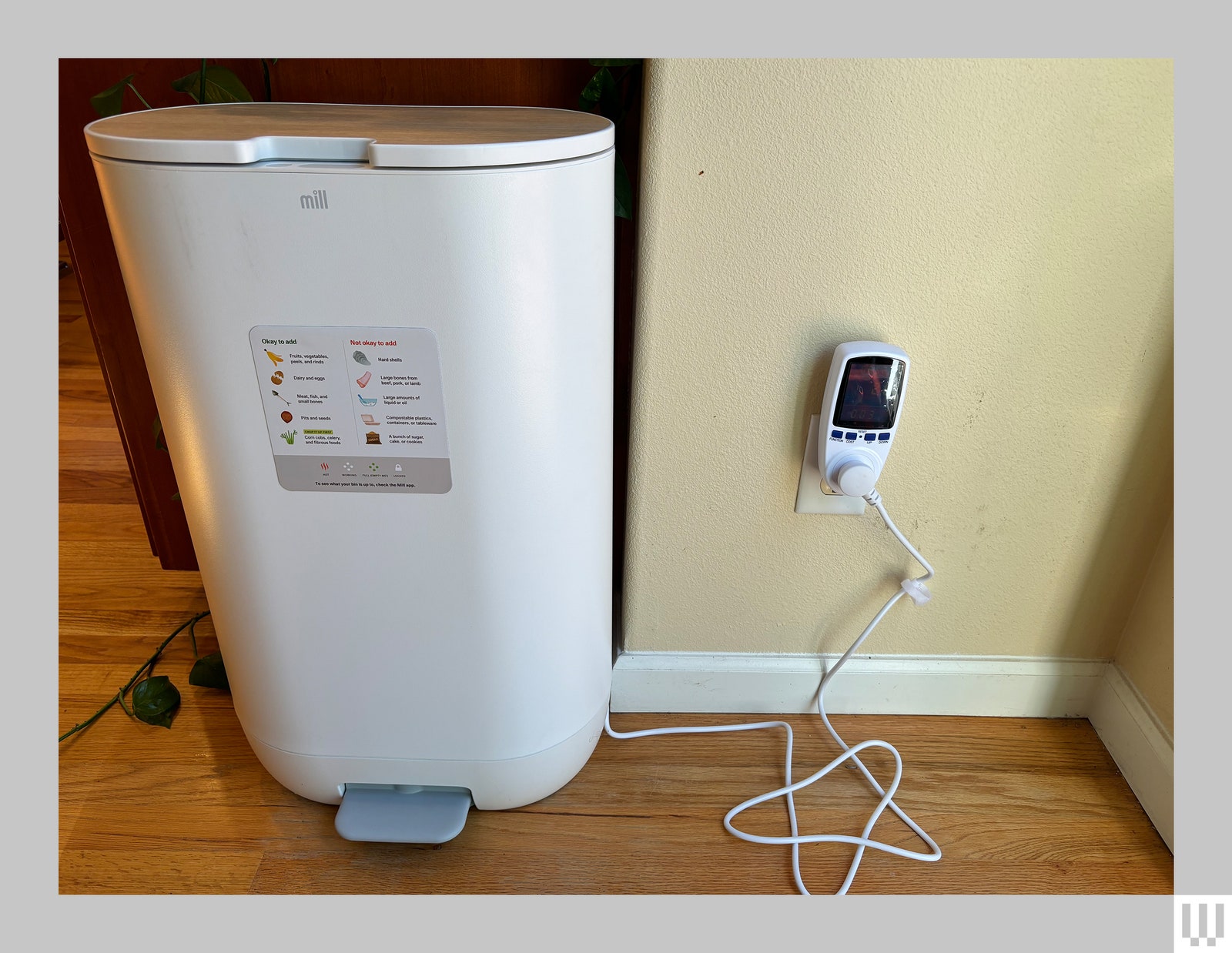 Tall machine for food recycling sitting in a kitchen up against a wall and plugged in