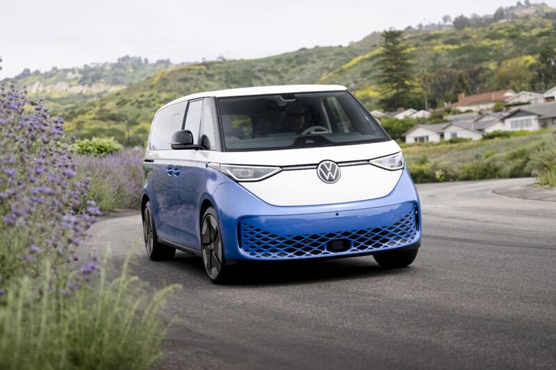 A white and blue VW ID Buzz drives along a road