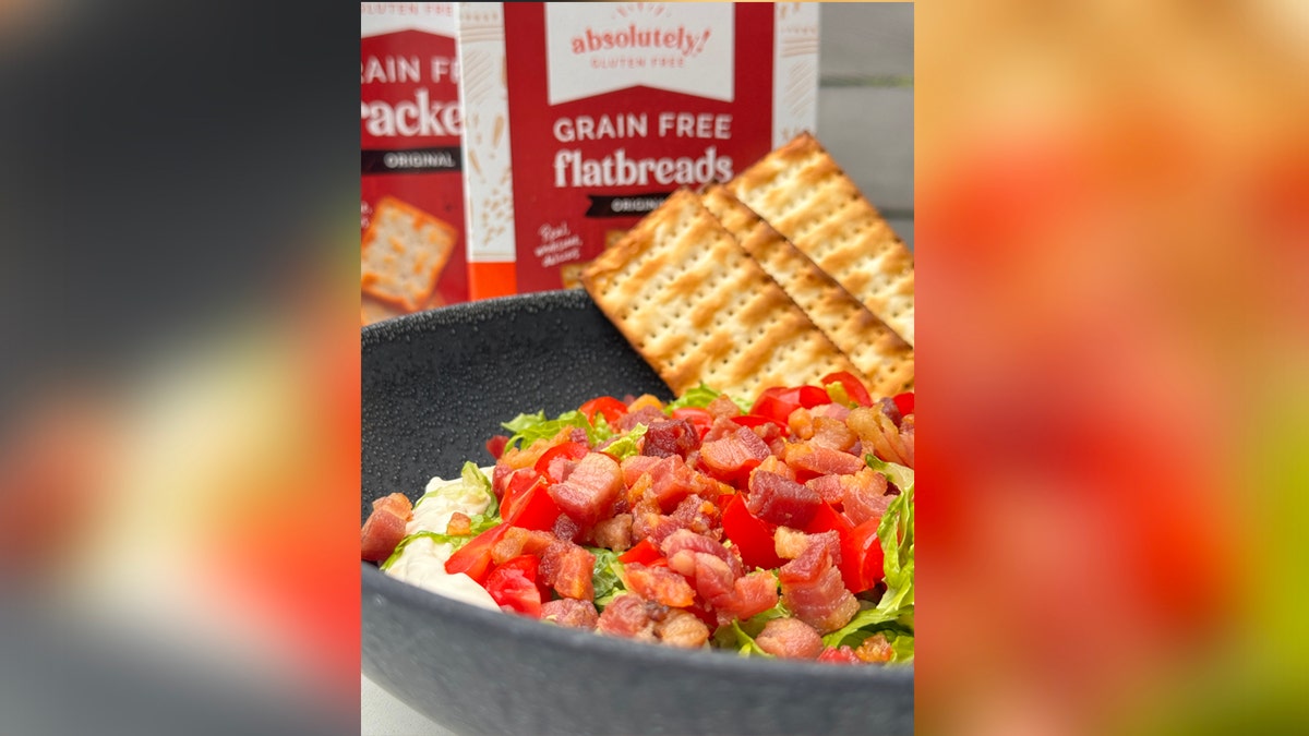 A BLT dip with chopped tomatoes, bacon, and lettuce. There are crackers in the dip/