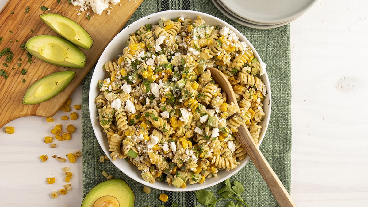 A bowl of "street corn" pasta salad with corn, avocado, cheese, and rotini pasta.