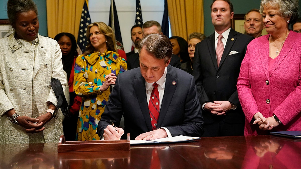 Virginia Gov. Glenn Youngkin, center, signs executive orders in the Governor's conference room as Lt. Gov. Winsome Earle-Sears, left, Suzanne Youngkin, second from left, Attorney General Jason Miyares, second from right, and Secretary of the Commonwealth, Kay Cole James, right, look on at the Capitol Saturday Jan. 15, 2022, in Richmond, Va. (AP Photo/Steve Helber)