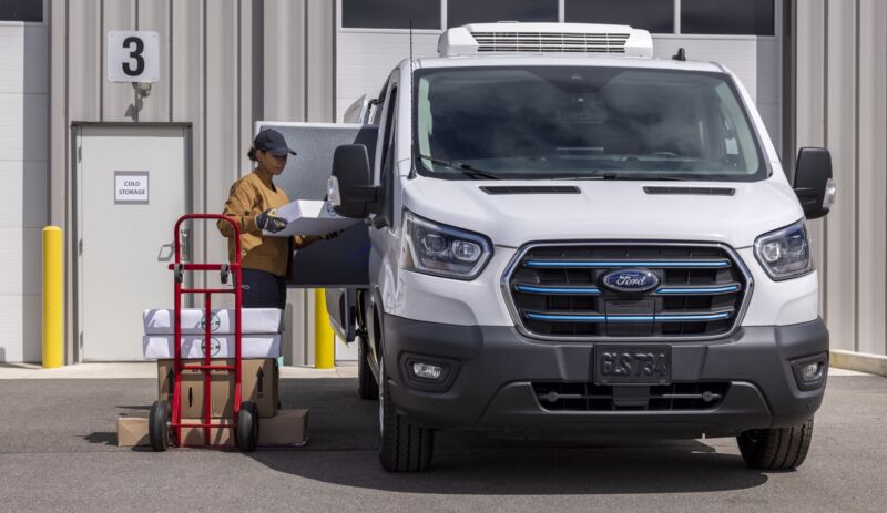 A woman loads things into the side of a Ford E-Transit that's been uplifted as a refrigerated van