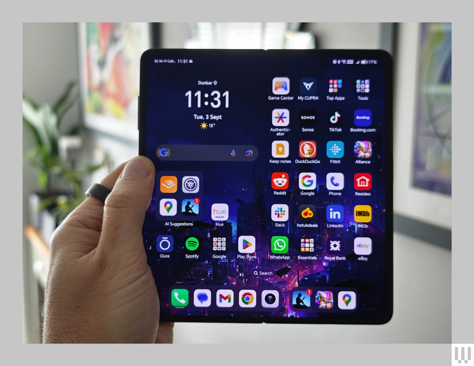 Hand holding a foldable mobile phone in the fully open position with the inner screen displaying app icons and the timedate