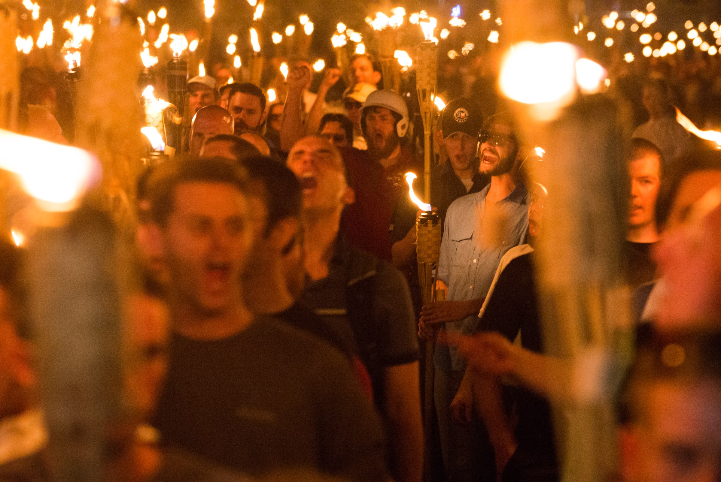 A crowd of young white men are yelling and holding tiki torches.