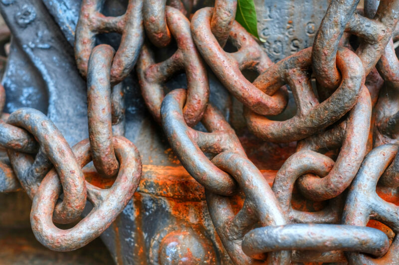 Rusty links of a chain, against an also-rusted metal background.