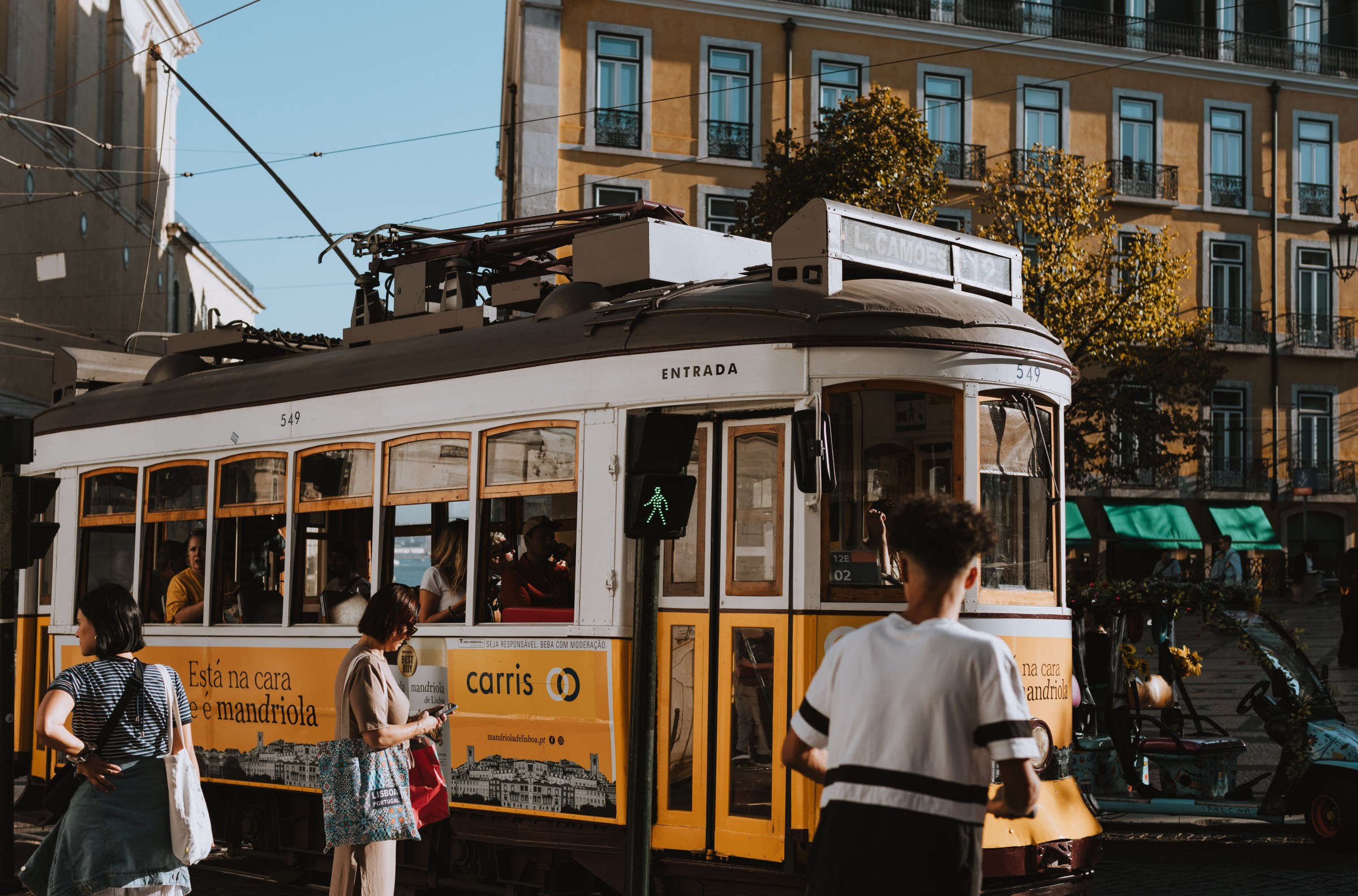 3 people in front of a yellow tram car in Portugal.